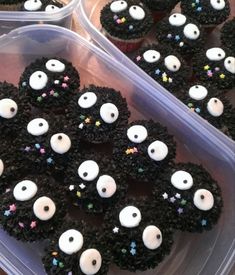 cupcakes decorated with black frosting and sprinkles are in plastic containers