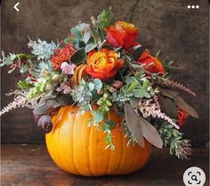 an orange pumpkin filled with flowers and greenery