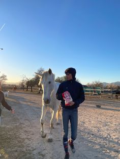 a man walking next to a white horse on a dirt road