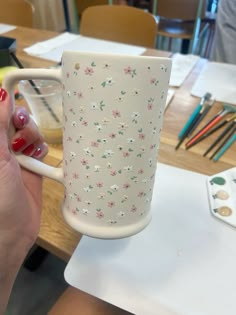 a woman holding a white coffee cup in her right hand with pink flowers on it