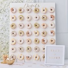 a white table topped with donuts next to a sign and vase filled with flowers