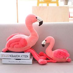 two pink stuffed flamingos sitting on top of a pile of books next to each other