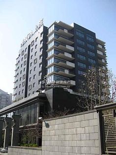 a tall building with lots of windows and balconies on the top floor is next to a concrete wall