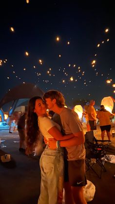 a man and woman kissing under an umbrella with lanterns in the sky above them at night