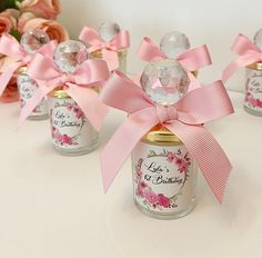 four small jars with pink bows on them and some flowers in the backgrouf