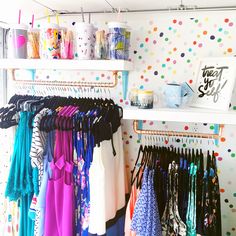 an organized closet with polka dot wallpaper and colorful clothing hanging on the shelves,