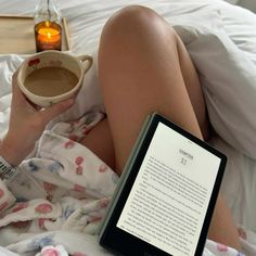 a woman laying in bed with her legs crossed holding a cup of coffee and an electronic book