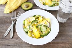 two white plates topped with cucumber and mango salad next to a glass of water