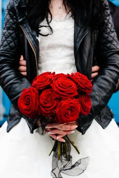 a woman in a white dress holding a bouquet of red roses and a black leather jacket