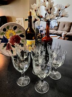 there are many wine glasses on the table next to a bottle and vase with flowers