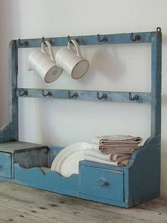 a blue shelf with two cups and plates on it, sitting next to a white wall