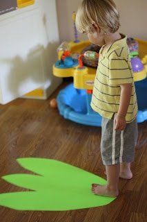 a young boy standing in front of a green frog shape cut out on the floor