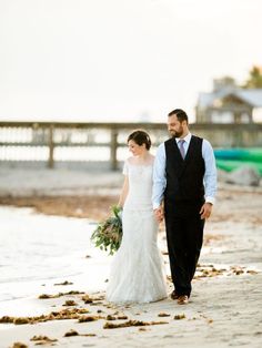 a bride and groom walking on the beach