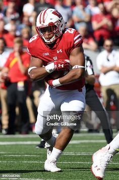 a football player running with the ball in his hand and people watching from the stands behind him