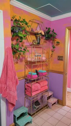 a bathroom with pink and purple walls, gold shelving and shelves filled with towels