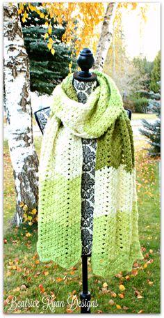 a green and white scarf sitting on top of a mannequin next to a tree