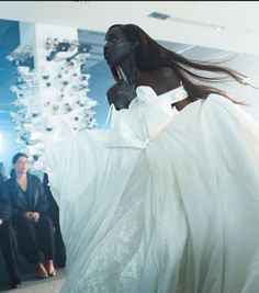 a woman in a white dress walking down a runway