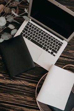 an open laptop computer sitting on top of a wooden table next to a notebook and pen