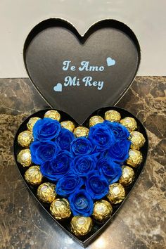 a heart shaped box filled with blue roses and chocolates on top of a table