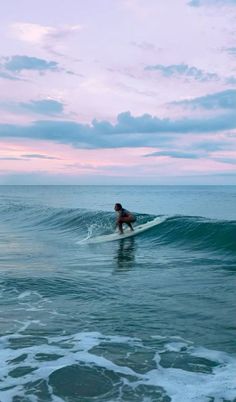 a person riding a surfboard on top of a wave in the ocean at sunset