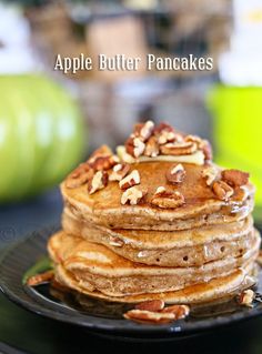 a stack of pancakes topped with nuts on top of a black plate next to an apple