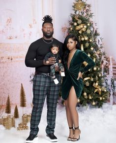 a man and woman standing in front of a christmas tree holding a small baby boy