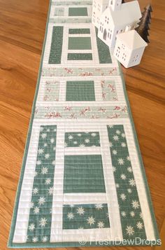 a quilted table runner with white houses and trees on the top, along with a wooden floor