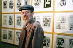 an old man with glasses and a hat standing in front of a wall full of comics