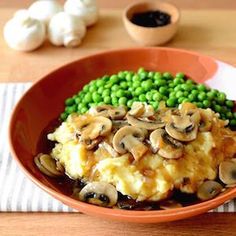 an orange bowl filled with mashed potatoes, peas and mushrooms