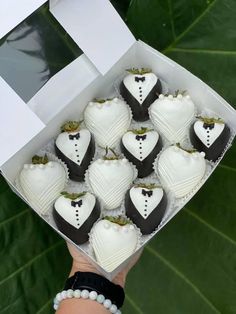 a hand holding a box filled with chocolate covered heart shaped treats on top of a green leafy background