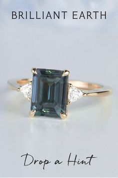 a ring with an emerald stone and two diamonds on the side, in front of a white