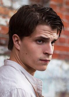 a close up of a person with a brick wall in the background and one hand on his hip