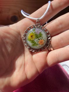 a woman's hand is holding a necklace with an image of flowers on it