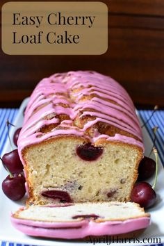 a loaf of cake with pink icing and cherries on top, sitting on a plate