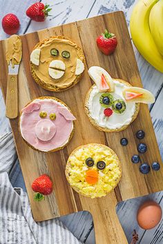 a wooden cutting board topped with food on top of a table next to bananas and strawberries