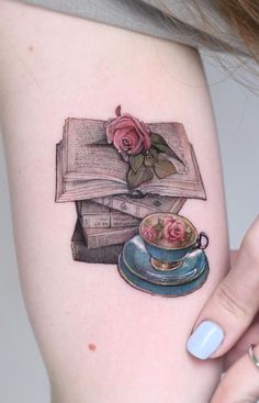 a woman's arm with a tattoo on it that has books and a teacup