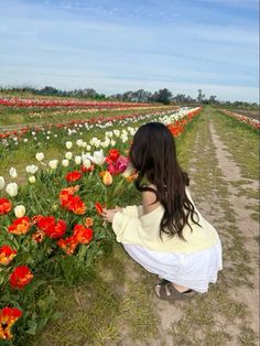 a woman kneeling down in the middle of a field full of flowers