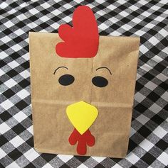 a brown paper bag with a chicken on it's face and red hair is sitting on a black and white checkered tablecloth