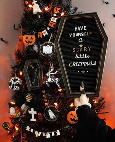 someone is decorating a halloween tree with black and orange decorations on the top, which reads have yourself scary little crememas