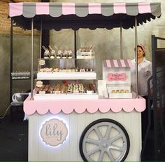 a woman standing behind a pink and white cart with cupcakes on it's sides