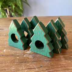 three green wooden houses sitting on top of a table next to a potted plant