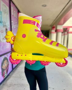 a woman holding up a yellow shoe shaped inflatable object with pink and purple accents