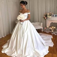 a woman in a white wedding dress standing on a wooden floor next to a fireplace