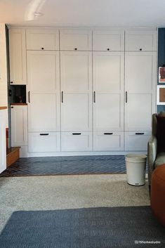 a living room filled with lots of white cabinets next to a brown chair and ottoman