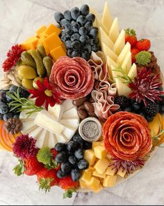 a platter filled with different types of cheeses and fruits on top of a marble table