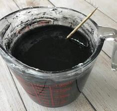 a black liquid in a measuring cup with a wooden stick sticking out of it