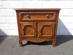 an old wooden cabinet sitting in front of a white brick wall on the side walk