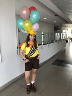 a woman in shorts and a yellow shirt is holding balloons on her head while standing next to a wall