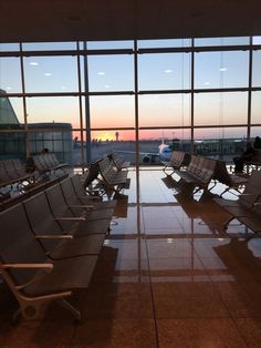 an airport terminal filled with lots of empty chairs next to a large window at sunset