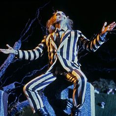 a man in striped suit and tie on stage with his hands out to the side